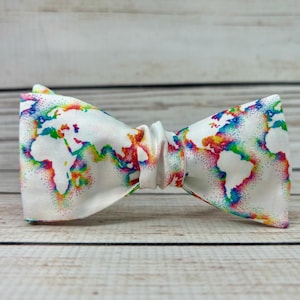 May include: A white bow tie with a rainbow world map print. The map is outlined in white and filled with rainbow colors.