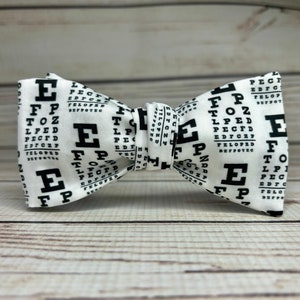 May include: A white bow tie with a black eye chart pattern. The pattern includes the letters E, FP, TOZ, LPED, PECFD, TELOPED, and EDFCZ.