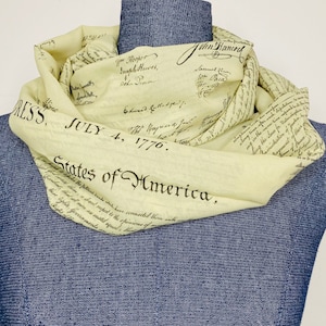 May include: A light yellow scarf with the text "JULY 4, 1776. States of America." printed on it. The text is in black and is a replica of the Declaration of Independence.