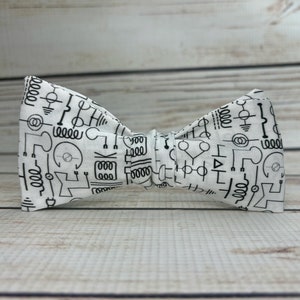 May include: A white bow tie with a black and white pattern of electrical circuit symbols.