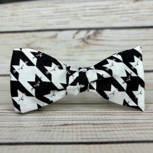 May include: A black and white bow tie with a houndstooth pattern and a repeating image of a cat face.