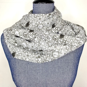 May include: A white scarf with a black and white pattern of a city map. The scarf is folded and displayed on a blue mannequin.