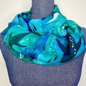 May include: A turquoise blue silk scarf with a black and white abstract design of fish and waves. The scarf is folded and displayed on a mannequin.