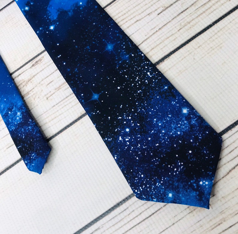 Tie front and end lay parallel angled into the corner of the frame. The necktie is shades of blue from deep navy to light blue swirled like deep space and scattered with round stars of varying sizes giving a depth effect.