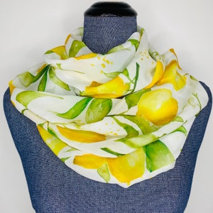 May include: A white silk scarf with a watercolor design of lemons and leaves. The lemons are yellow and the leaves are green.