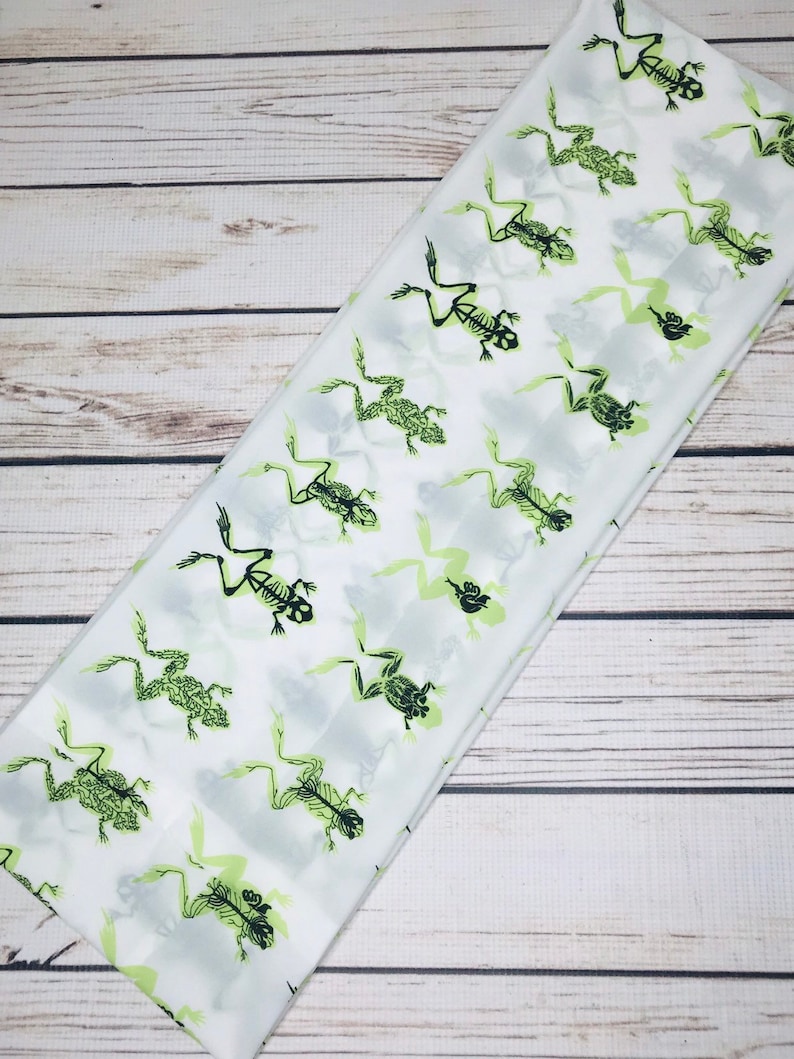 May include: White fabric with a repeating pattern of green skeleton frogs. The frogs are in various poses, some are jumping, some are sitting, and some are swimming.