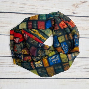 May include: A black and green scarf with a print of book titles and covers. The scarf is made of a soft, lightweight fabric and is perfect for adding a touch of style to any outfit.