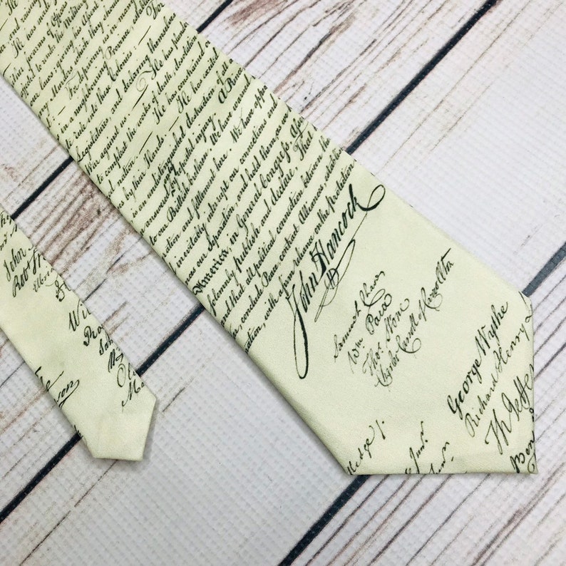 Tie front and end lay parallel angled into the corner of the frame. the necktie is an old parchment color with deep brown lettering. The lettering is a copy of the declaration of independence in its original script with signatures a the bottom.