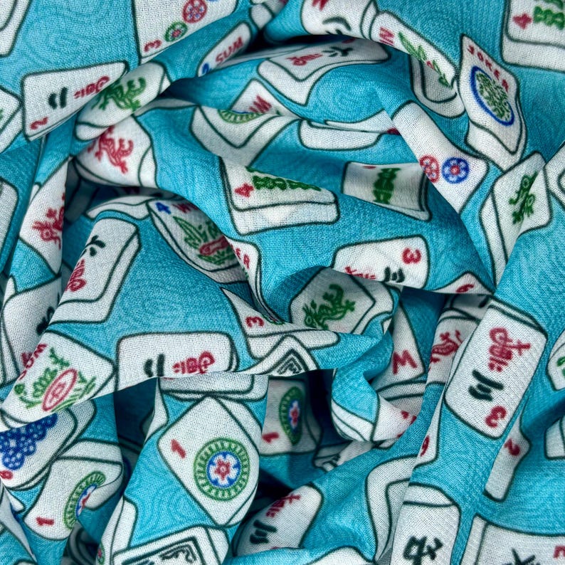 Op de afbeelding: Een turquoise stof met een wit patroon van mahjong-tegels. De tegels hebben Chinese karakters en symbolen.