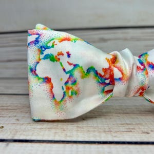 May include: A white bow tie with a rainbow colored world map design. The map is made up of small dots.
