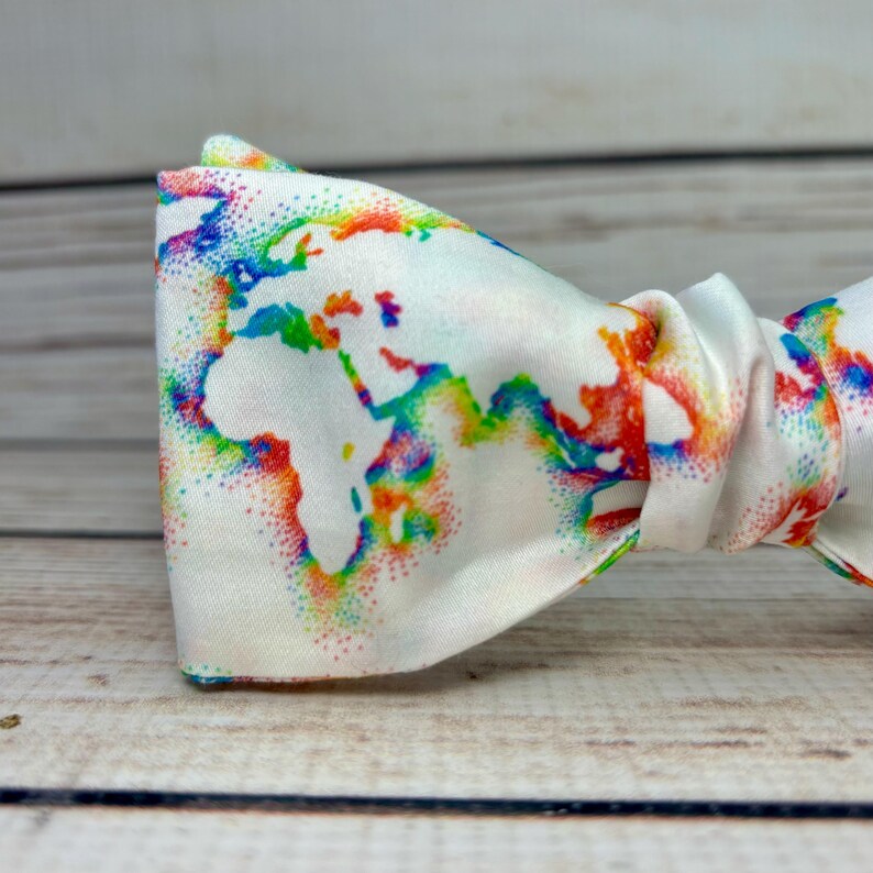 May include: A white bow tie with a rainbow colored world map design. The map is made up of small dots.