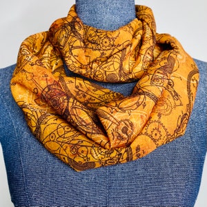 May include: A gold and brown infinity scarf with a vintage steampunk design featuring intricate gears and clockwork patterns.