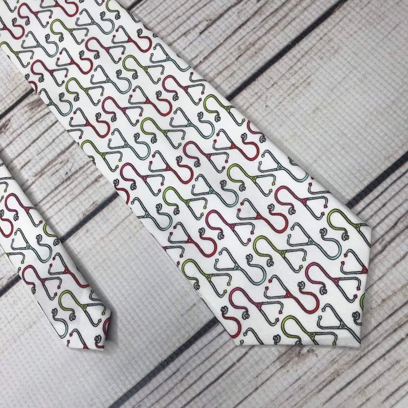 Tie front and end lay parallel angled into the corner of the frame. White background with tiny red and green stethoscopes in rows, each row has a stethoscope facing up and another facing down repeated across the row.