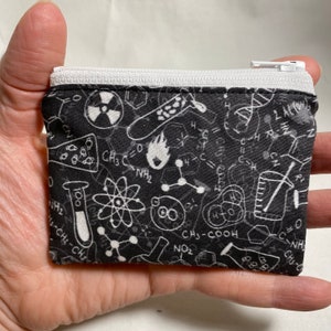 May include: A black zippered pouch with a white zipper. The pouch is covered in a white pattern of scientific symbols and formulas, including atoms, molecules, beakers, and test tubes.