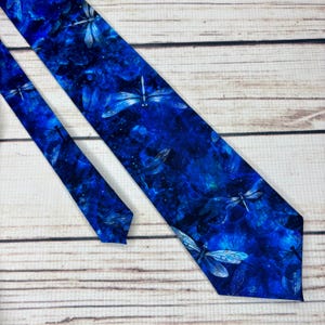 May include: A blue necktie with a pattern of dragonflies. The tie has a dark blue background with lighter blue dragonflies scattered across the fabric. The tie is made of a smooth material and is suitable for formal or semi-formal occasions.