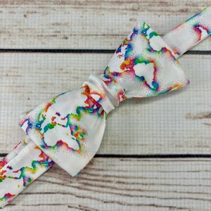 May include: A white bow tie with a rainbow world map print. The map is outlined in white and filled with rainbow colors.