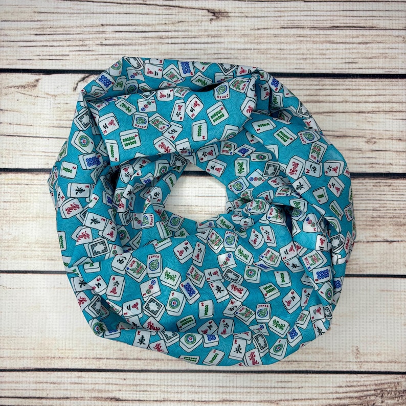 Op de afbeelding: Een turquoise blauwe sjaal met een witte achtergrond en een herhalend patroon van mahjong-tegels.