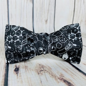 May include: A black bow tie with a white science pattern. The pattern includes chemical formulas, atoms, and other science-related symbols.
