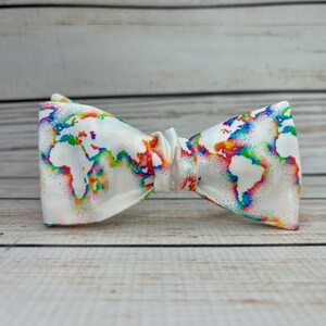 May include: A white bow tie with a rainbow world map print. The map is outlined in white and filled with rainbow colors.