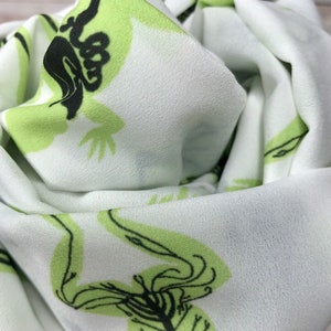 May include: White fabric with a green and black skeletal frog print. The fabric is soft and has a subtle sheen.