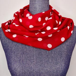 May include: A red scarf with white polka dots is draped around a mannequin's neck. The scarf is made of a soft fabric and has a classic polka dot pattern. The scarf is a versatile accessory.