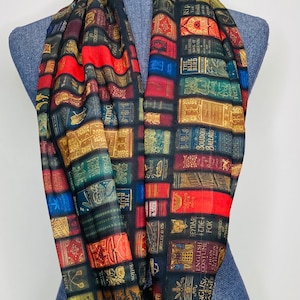May include: A black infinity scarf with a print of colorful book spines. The scarf features a variety of book titles, including "The Blue Bird", "Boudoir Ballads", "All About Ships", and "Classic Myth & Legend".