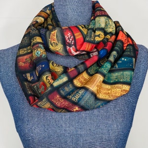 May include: A colorful infinity scarf featuring a pattern of vintage book covers with titles like "Blue Birds", "Ballads", and "Sylvanus", printed on a black background.