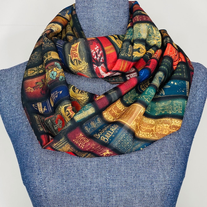 May include: A colorful infinity scarf featuring a pattern of vintage book covers with titles like "Blue Birds", "Ballads", and "Sylvanus", printed on a black background.