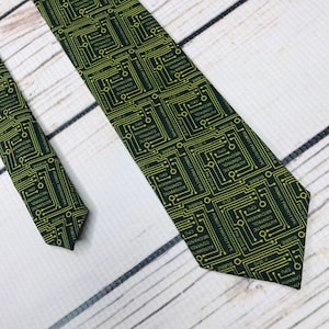 May include: A black necktie with a repeating pattern of yellow circuit boards. The text on the circuit boards reads "ROBOT PROTOTYPE", "AUTOMATIC CONTROL MECHANISM", "CPU", "BUBBIE", and "PH-2010".