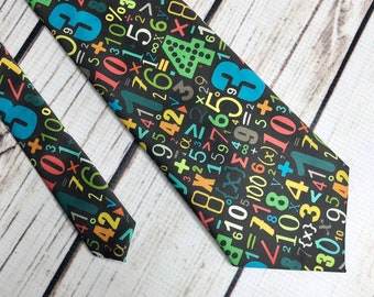 Puede incluir: Una corbata negra con un patrón colorido de números, símbolos matemáticos y ecuaciones. Los números son de varios colores, incluyendo azul, verde, amarillo y rojo. La corbata está hecha de una tela suave.