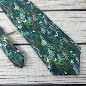 May include: A dark green tie with a repeating pattern of white birds and green trees.