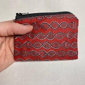 May include: A red zippered pouch with a black zipper and a black and white DNA pattern.