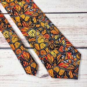 May include: A necktie featuring a repeating pattern of monarch butterfly wings in vibrant shades of orange, yellow, and black. The design covers the entire surface of the tie, showcasing the intricate vein details and white-spotted black borders.