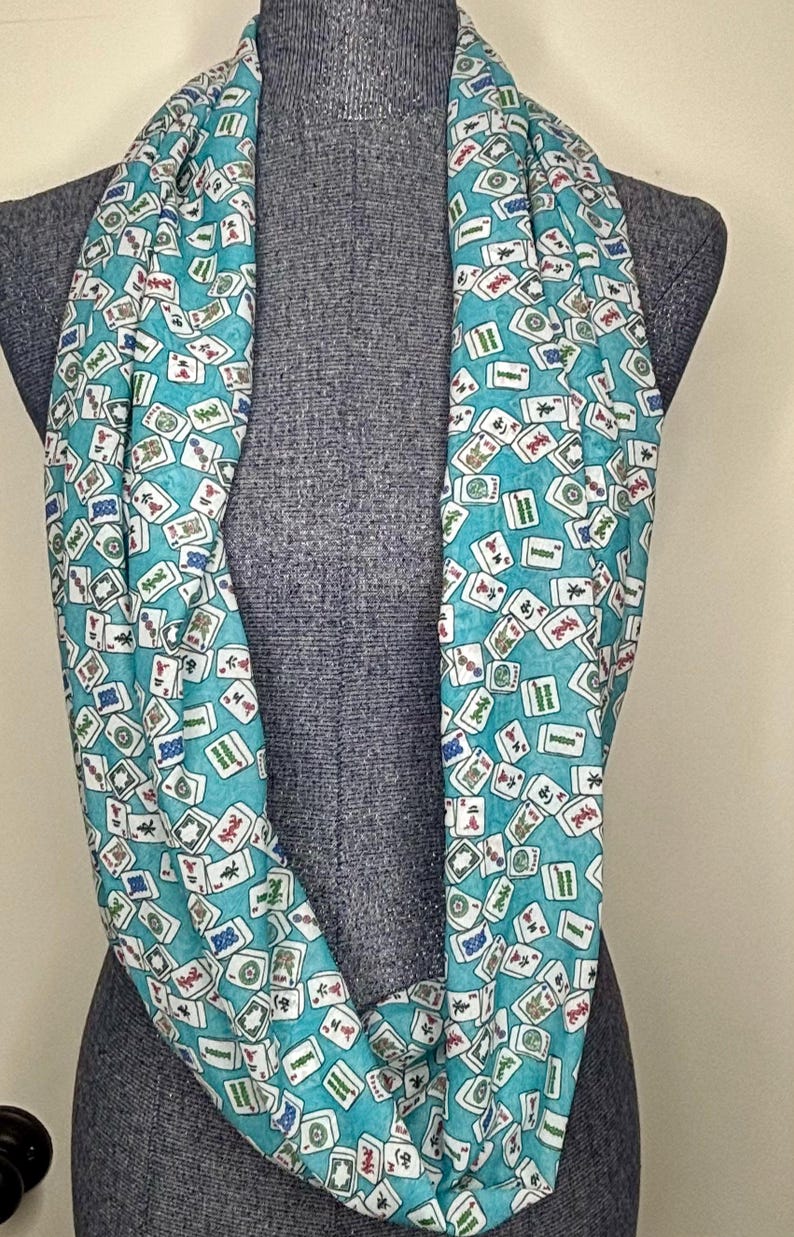 Op de afbeelding: Een turquoise oneindige sjaal met een witte achtergrond en een patroon van mahjong-tegels. De tegels zijn willekeurig over de sjaal verspreid.