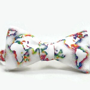 May include: A white bow tie with a colorful world map print. The map is outlined in white and filled with rainbow colors.