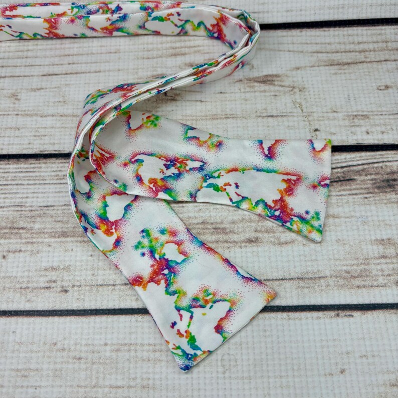 May include: A white bow tie with a colorful world map print. The map is outlined in rainbow colors and has a white background.