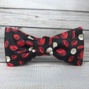 May include: A black bow tie with a pattern of red blood cells and white blood cells.