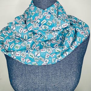 Op de afbeelding: Een turquoise blauwe sjaal met een witte achtergrond en een patroon van mahjong-tegels. De tegels zijn willekeurig over de sjaal verspreid en bevatten Chinese karakters en symbolen.
