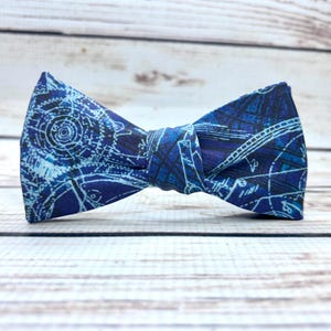 May include: A blue bow tie with a white and blue patterned design of gears and other mechanical elements.