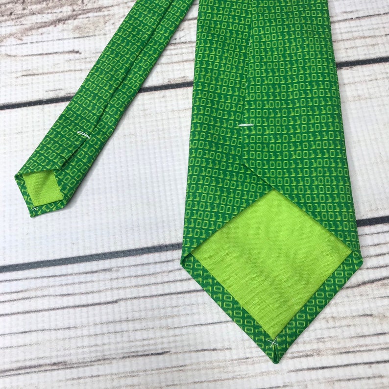 K&ouml;nnte beinhalten: Eine gr&uuml;ne Krawatte mit einem Muster aus wiederholtem Bin&auml;rcode, 1010101, in einem helleren Gr&uuml;nton.