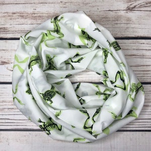 May include: White infinity scarf with a repeating pattern of green skeleton frogs.