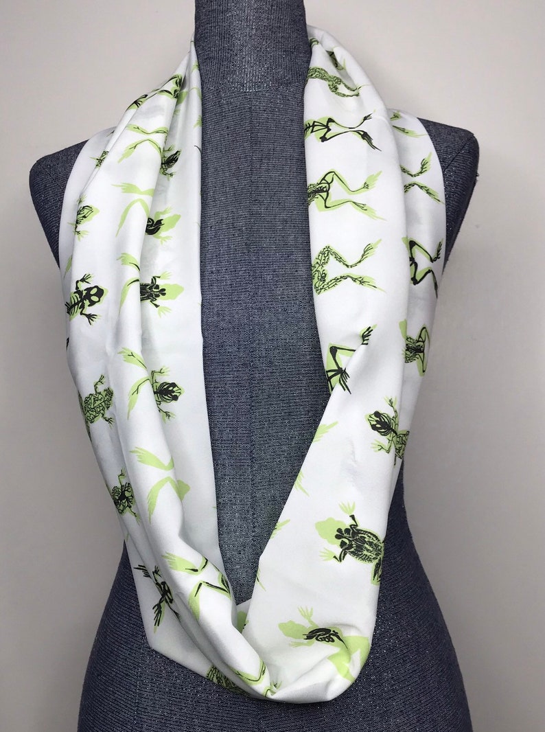 May include: White infinity scarf with a repeating pattern of green frog skeletons.