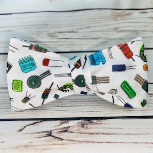 May include: White bow tie featuring a pattern of colourful electronic components, such as resistors, capacitors, and integrated circuits.