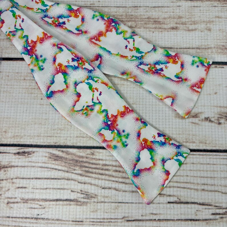 May include: A white bow tie with a colorful world map pattern. The map is outlined in white and filled with rainbow colors.
