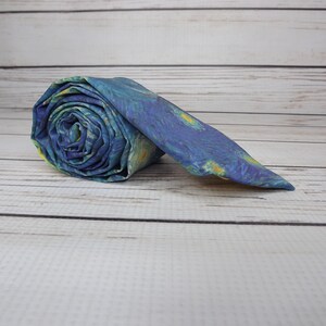May include: A blue and yellow patterned tie rolled up on a white wooden surface.