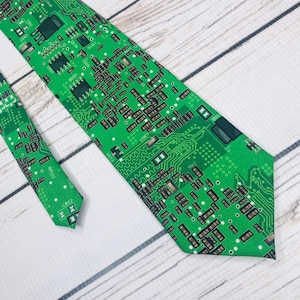May include: Green necktie with a circuit board pattern. The tie is made of a smooth fabric and has a pointed tip.