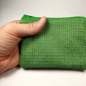 May include: A green zippered pouch with a repeating pattern of yellow binary code. The pouch is made of a soft, fabric material.