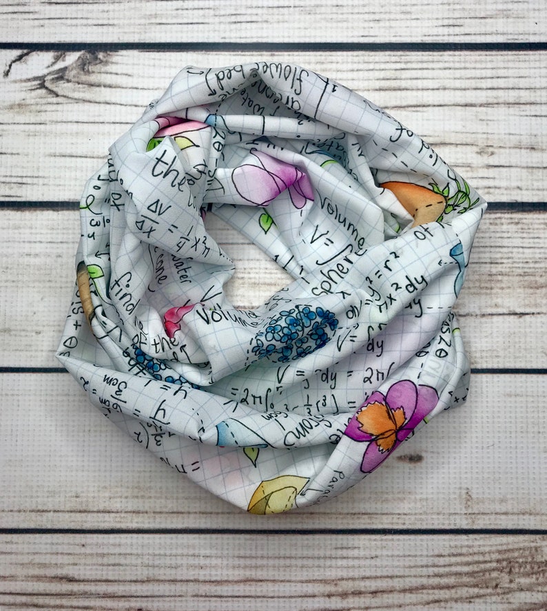 Op de afbeelding: Een witte oneindigheidssjaal met een rasterpatroon en kleurrijke bloemen en wiskundige vergelijkingen erop gedrukt. De vergelijkingen omvatten het volume van een bol, het volume van een kegel en de integraal van een functie.