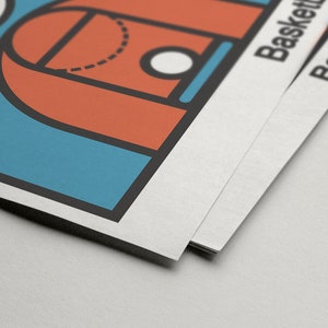 May include: A stack of basketball-themed posters. The top poster features a basketball court design in orange, blue, and black. The word "Basketball" is printed on the side of the posters.