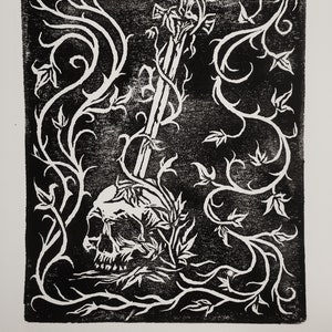 May include: A black and white linocut print of a skull with a sword growing through it, surrounded by vines.